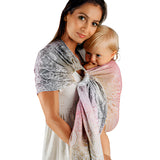 Woman holding a child wrapped in a patterned wrap against a gray wall.