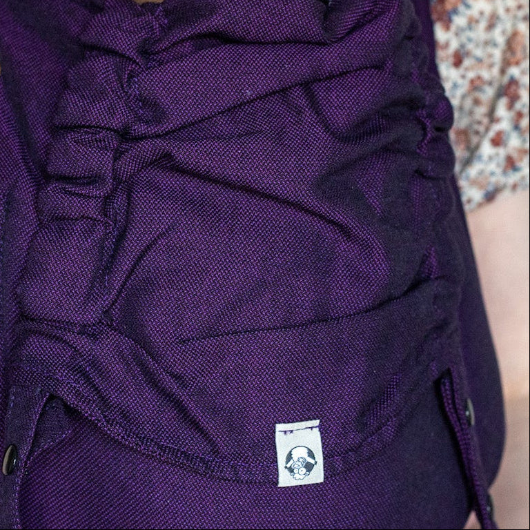 Person holding a baby in a purple baby carrier against a plain background