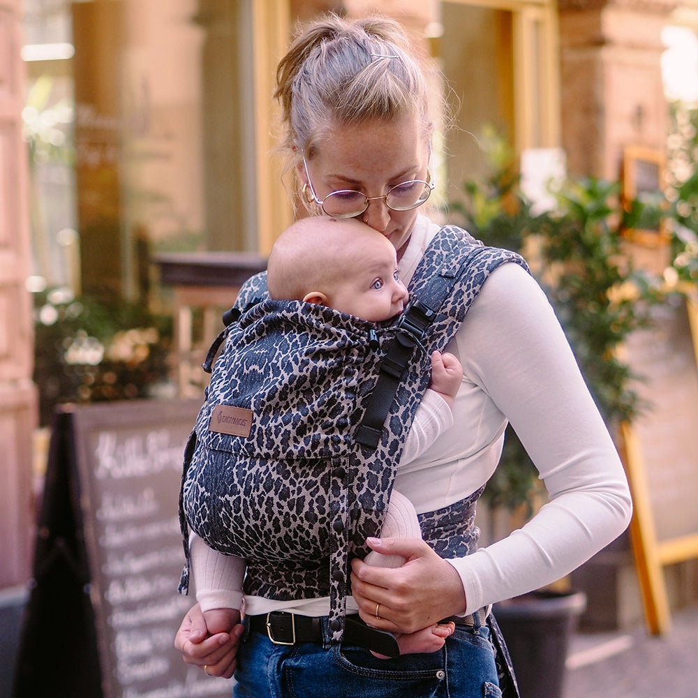 Woman carrying a baby in a leopard print baby carrier outdoors.