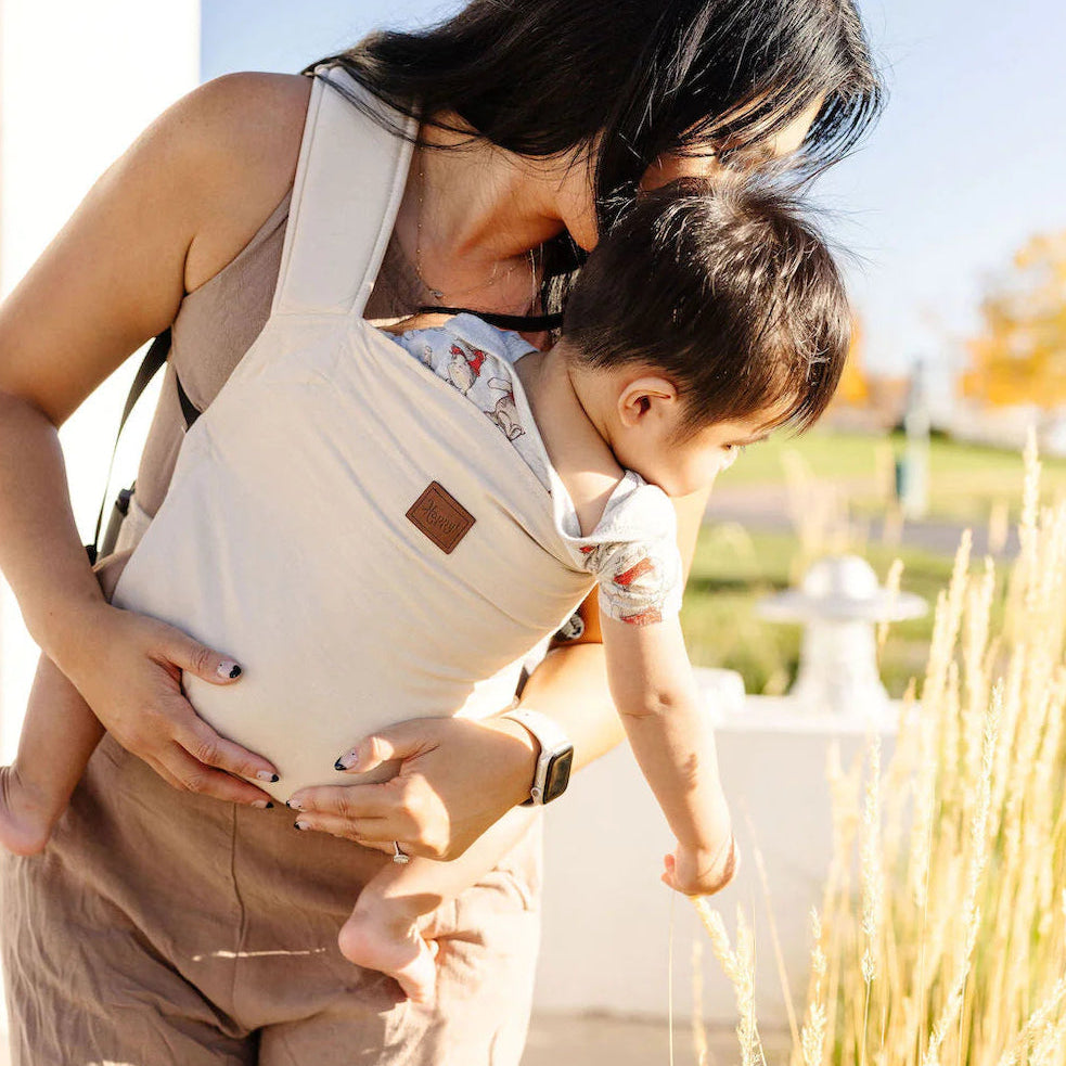 Woman holding a child in a baby carrier outdoors on a sunny day.