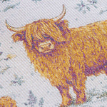 Close-up of a woven textile featuring Highland cows in golden yellow and brown tones on a light off-white background with muted blue-gray floral details.