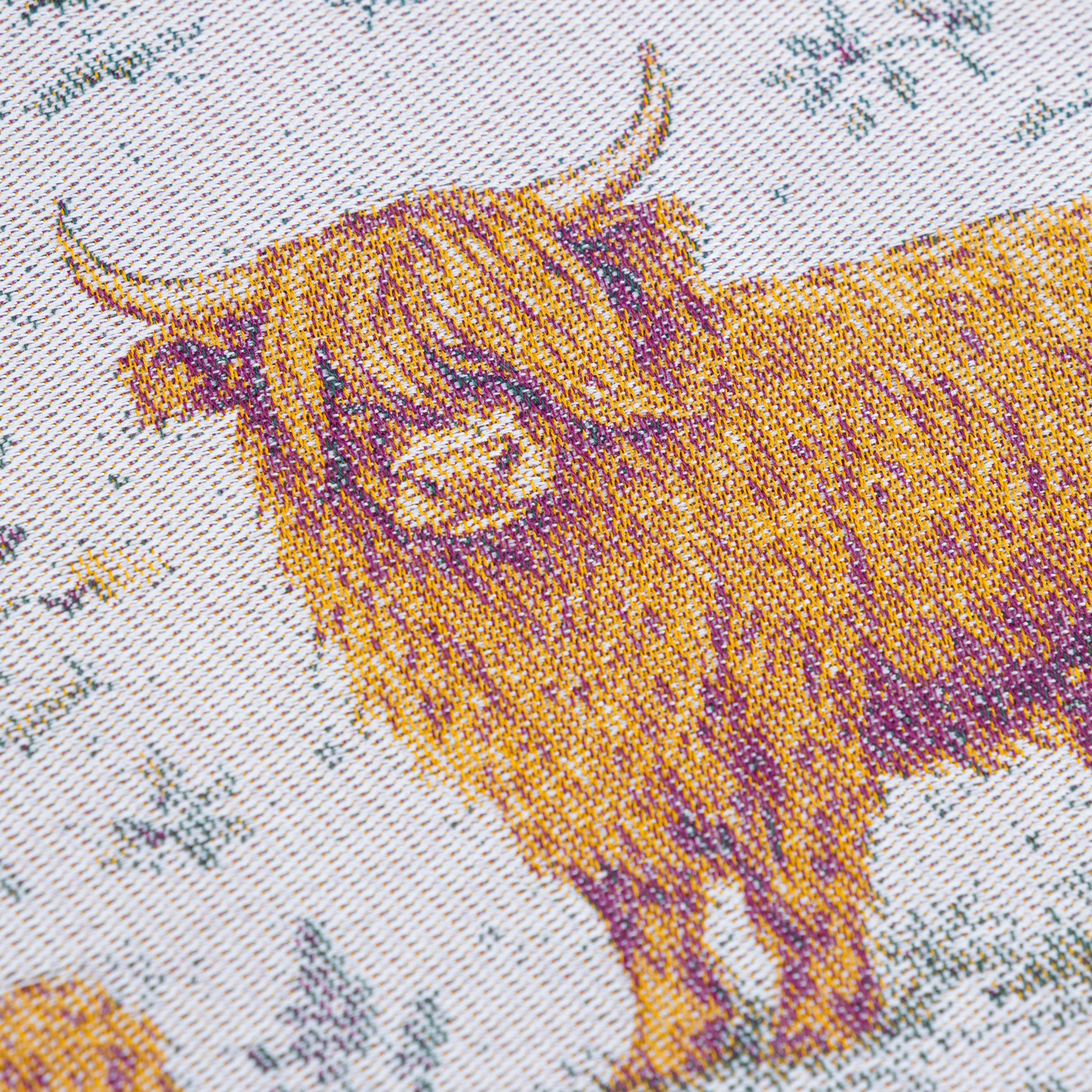 Close-up of a woven textile featuring Highland cows in golden yellow and brown tones on a light off-white background with muted blue-gray floral details.