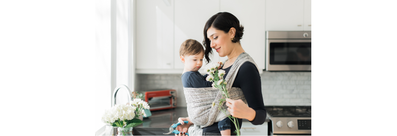 Woman holding flowers and a child in a kitchen